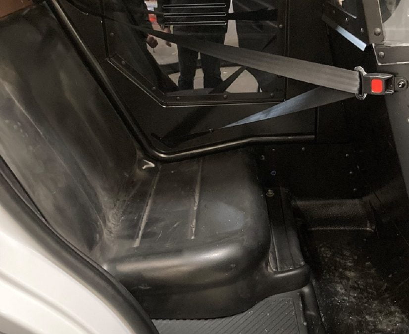 Interior of a small vehicle showing a black plastic seat with a seatbelt. The surroundings appear industrial.