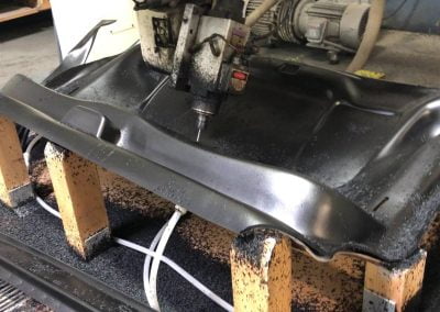 A CNC machine meticulously cuts a metallic automotive part, surrounded by metal shavings, while the adjacent seating systems undergo quality checks.