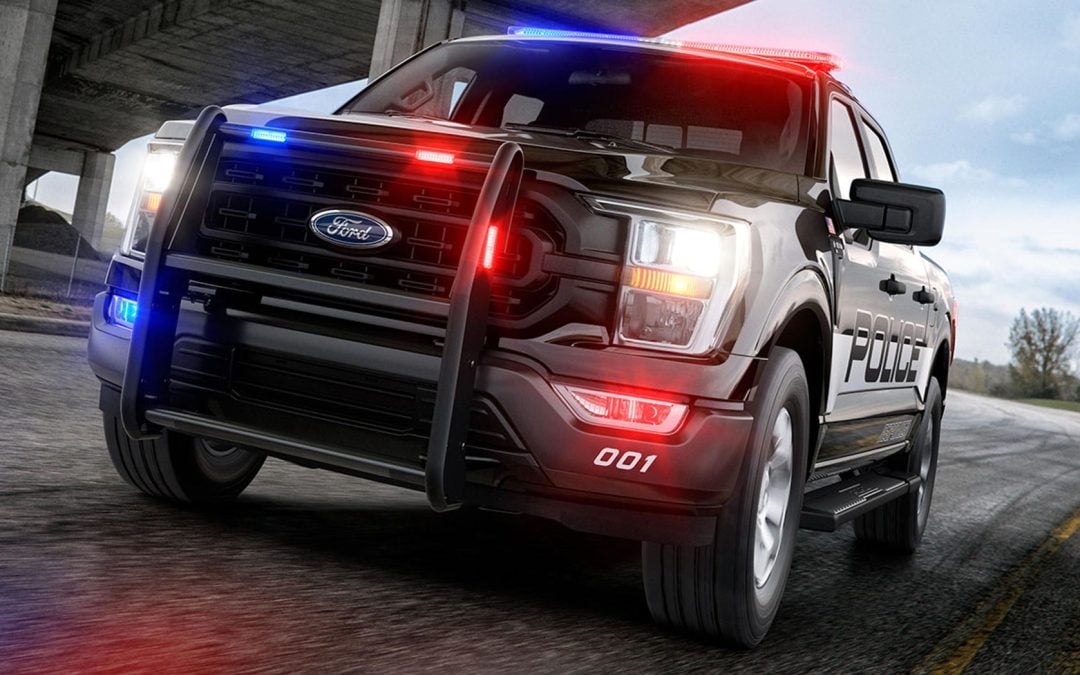 A black police truck with flashing red and blue lights, a crucial element of transport systems, drives on a road beneath an overpass.
