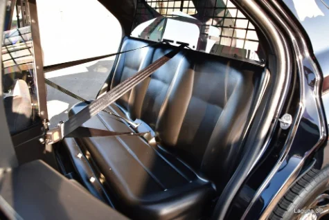 Backseat of a vehicle with a seatbelt restraint system and a partition separating the driver's area from the rear seat, featuring durable prisoner seat covers for added security and protection.